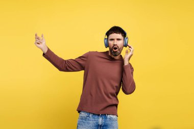 Orta yaşlı, çekici bir adamın portresi kulaklıkla müzik dinleyen, dans eden, kameraya bakan, sarı arka planda izole edilmiş. Eğlenceli konsept