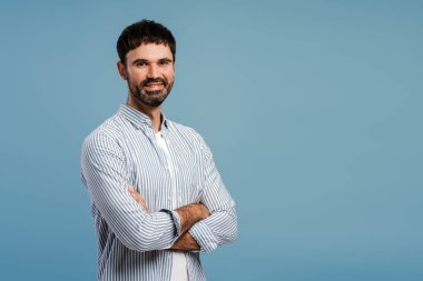 Başarılı, kollarını kavuşturmuş, gülümseyen sakallı adam, kameraya bakıyor, mavi arka planda tek başına duruyor, kopyalama alanı. Stüdyoda poz veren bir iş adamı. İş konsepti