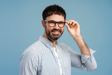 Gülümseyen, orta yaşlı, şık gözlükler takan, başka tarafa bakan, mavi arka planda poz veren yakışıklı bir adamın portresi. Tedavi, reklam görme konsepti