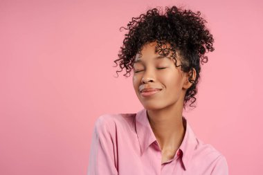 Güzel, gülümseyen Afro-Amerikan kadın gülümseyen ve pembe arka planda kapalı gözlerle poz veren. Halk konsepti 