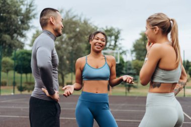 Gülümseyen, çeşitli, çok ırklı kadınlar ve şık spor giysiler giyen, konuşan, dışarıda birlikte antrenman yapan bir grup erkek. Takım çalışması, iletişim konsepti