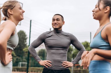 Bir grup mutlu, çeşitli, çok ırklı kadın ve erkek şık spor giysiler giyiyor, konuşuyor, sokakta, dışarıda birlikte antrenman yapıyorlar. Takım çalışması, iletişim konsepti