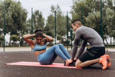 Aktif, gülümseyen Afrikalı Amerikalı kadın portresi. Sokakta, dışarıda kişisel antrenörle karın kasları eğitimi alıyor. Sağlıklı yaşam tarzı, motivasyon kavramı