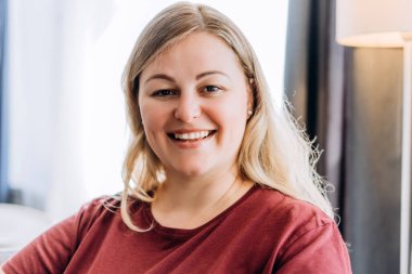 Evde kameraya poz veren pozitif beyaz kadın portresi.