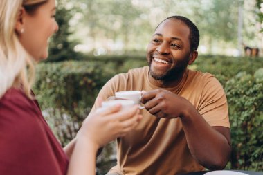 Kafede bir kadınla buluşurken kahve içen mutlu, Afro-Amerikan bir adam.