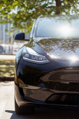 Şehrin caddesinde park edilmiş şık siyah elektrikli araba temiz enerjisi ve güçlü tasarımıyla yenilik ve çevre bilincini sembolize ediyor.