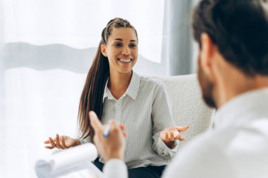 Gündelik kıyafetler giyen, işaret diliyle konuşan, modern ofiste otururken el kol hareketi yapan çekici İspanyol kadın ve erkeğin portresi. İletişim konsepti