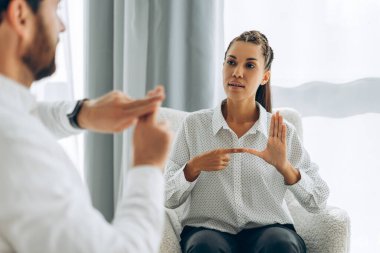 Çekici İspanyol kadın sakallı adamla konuşuyor, işaret diliyle el kol hareketi yapıyor, modern ofiste oturuyor. İletişim konsepti