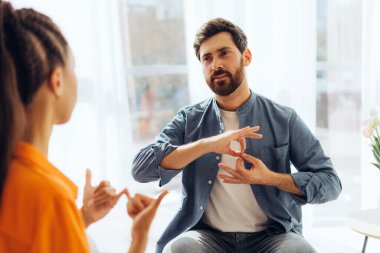 Pozitif sakallı adam portresi ve çekici gülümseyen İspanyol kadın, çevirmen, evdeki rahat kanepede oturmuş işaret diliyle konuşuyor. İletişim konsepti