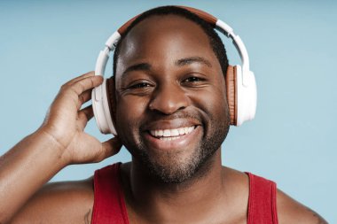 Portrait of smiling sporty African American man wearing wireless headphones for listening music, looking at camera in studio