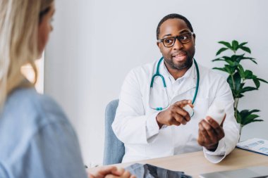 Gözlüklü bir erkek doktor klinikte ilaç yazan genç bir kadın için tıbbi danışmanlık yapıyor. Sağlık, tıp konsepti