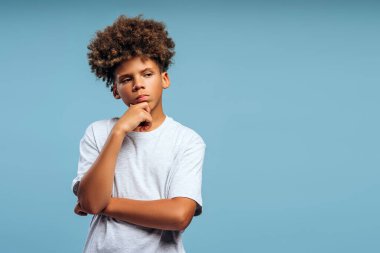 Kıvırcık saçlı, mavi arka planda yalnız poz veren yakışıklı Afro-Amerikan çocuk portresi. Reklam kavramı