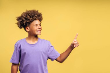 Mutlu, pozitif, kıvırcık saçlı Afro-Amerikan çocuğun fotokopi alanını gösteren portresi, başka yöne bakıyor. Sarı arka planda izole edilmiş bir model. Reklam kavramı