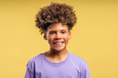 Sarı arka planda izole edilmiş fotoğraf makinesine bakan kıvırcık saçlı mutlu Afro-Amerikan çocuk portresi. Reklam kavramı