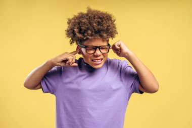 Sarı arka planda izole edilmiş kulakları gözlüklü, kıvırcık saçlı, üzgün Afrikalı Amerikalı çocuğun portresi. Ruh sağlığı, otizm konsepti