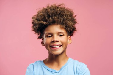 Otantik, gülümseyen, kıvırcık saçlı, pembe arka planda izole edilmiş kameraya bakan Afro-Amerikan çocuğun portresi. Reklam kavramı
