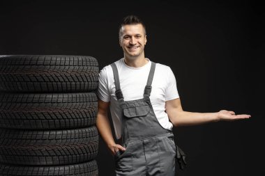 Gülümseyen tamirci satılık yeni kış lastiklerini sunuyor. Karlı yollarda güvenlik ve performans sağlıyor.