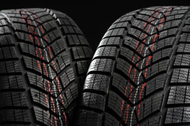 Winter car tires with red and white lines on tread pattern are standing on black background, ready for winter driving clipart