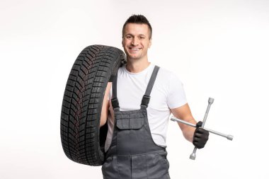 Gülümseyen tamirci lastik ve bijon anahtarı tutuyor, lastik değiştirmeye hazır, beyaz arka planda izole edilmiş.