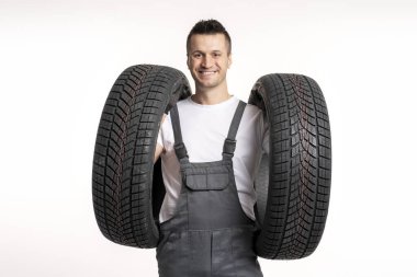 Gülümseyen bir tamircinin portresi iki yeni lastik tutuyor, garajında araba tekerleklerini değiştirmeye hazır.