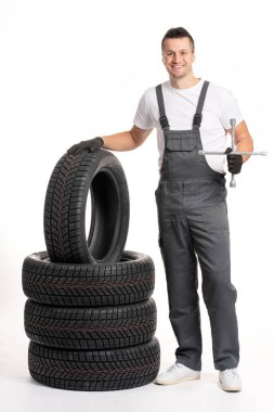 Gülümseyen tamirci İngiliz anahtarı tutuyor ve beyaz arka plandaki lastik yığınına yaslanıyor