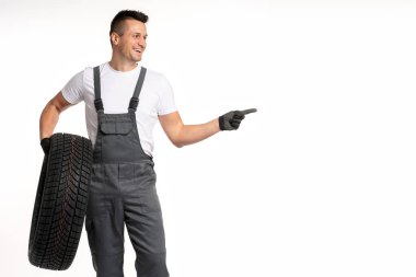 Gülümseyen tamirci beyaz bir arka planda tekerleği tutuyor ve parmağıyla çerçevenin sağ tarafını işaret ediyor.