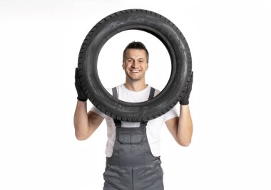 Gülümseyen tamircinin bir lastiği var, beyaz arka planda araba servisi uzmanlığı gösteriyor. Garajdaki profesyonel işçi bakım çalışmalarının önemini vurguladı