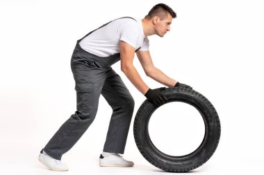Siyah eldiven giyen tamirci beyaz arka planda büyük bir lastik itiyor, lastik ve otomotiv bakımını temsil ediyor.