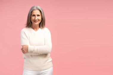 Gülümseyen, güzel, yaşlı, beyaz kazak giyen, kollarını çapraz yapıp kameraya bakan, pembe arka planda izole edilmiş, fotokopi çeken bir kadın portresi. Reklam kavramı