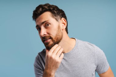 Portrait of handsome, bearded Latin man looking in mirror, cosmetology procedures isolated on blue background. Barber, morning routine concept clipart