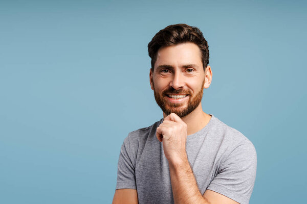 Handsome, smiling latin man wearing blue shirt looking at camera standing isolated on blue background. Successful businessman in studio. Shopping, advertisement concept