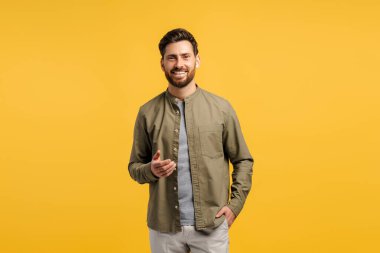 Mutlu, pozitif, sakallı, sıradan gömlekler giyen, kameraya bakan, sarı arka planda yalnız poz veren bir adamın portresi. Reklam, alışveriş konsepti