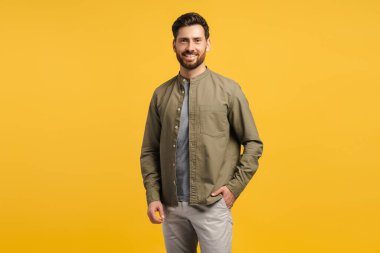 Yakışıklı, gülümseyen, sakallı, sıradan kıyafetler giyen, kameraya bakan, sarı arka planda izole edilmiş pozlar veren Latin bir adamın portresi. Moda modeli stüdyoda poz veriyor. Reklam, alışveriş konsepti