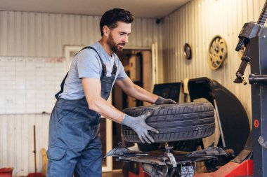 Profesyonel, yakışıklı, gülümseyen adam, tekerlek tutan işçi, modern benzin istasyonunda çalışıyor. Reklam kavramı