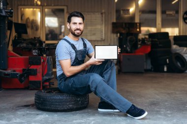 Mutlu, yakışıklı, kendine güvenen bir adamın portresi, profesyonel bir tamirci, dijital tableti boş bir ekranla tutuyor ve kameraya bakıyor. Reklam kavramı