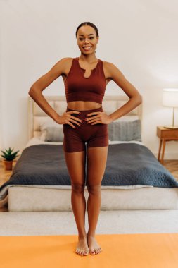 Evdeki yatak odasında spor minderinde poz veren Afro-Amerikan kadın. Kameraya bakıyor. Ev sporu. Sağlıklı yaşam tarzı kavramı