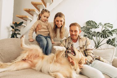 Gülümseyen, mutlu baba ve geveze, rahat koltukta oturan küçük kız evde Golden Retriever ile oynuyor. Aşk hayvanı konsepti