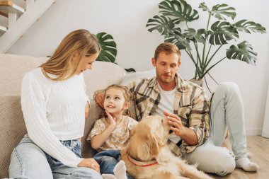 Güzel gülümseyen bir aile, mutlu bir anne, baba ve tatlı bir kız evcil Golden Retriever 'la rahat koltukta oturuyor. Ebeveynlik kavramı, aşk