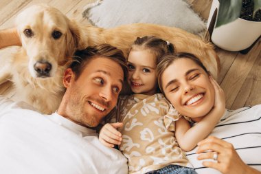 Gülümseyen, güzel aile ve Golden Retriever birbirine sarılıyor, yalan söylüyor, evdeki rahat oturma odasında kucaklaşıyor. Hayvan, evcil hayvan aşkı konsepti
