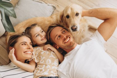Mutlu aile portresi, güzel anne, baba, sevimli küçük kız köpekle birlikte oynuyorlar, Golden retriever, evdeki rahat oturma odasında. Hayvan bakımı, hayvan konsepti.