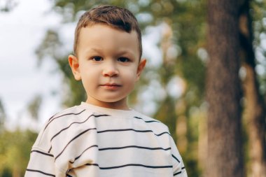 Gülümseyen küçük çocuğun portresi kameraya bakıyor, dışarıda poz veriyor, parkta duruyor. Reklam kavramı