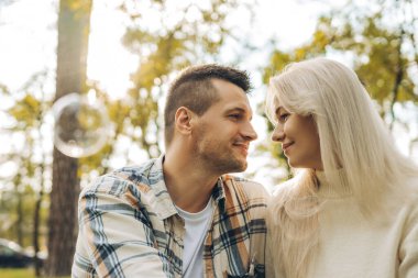 Gülümseyen mutlu bir çiftin portresi, güzel bir kadın ve erkek birbirine sarılıyor, dışarıda, parkta birbirine bakıyor. İlişki, sonbahar, flört kavramı