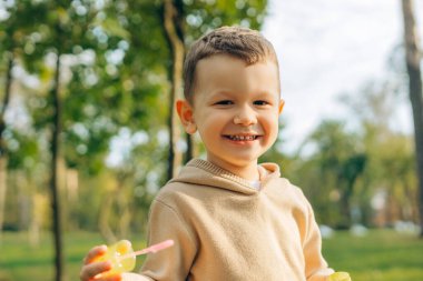 Gülümseyen küçük bir çocuğun portresi, parkta dikilen çocuk, dışarıda poz veren kameraya bakıyor. Çocukluk kavramı