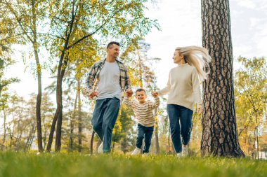 Mutlu bir ailenin portresi, güzel bir anne, gülümseyen bir baba ve küçük bir oğul birlikte parkta yürüyorlar. İlişki, rahatlama, ebeveynlik, çocukluk kavramı