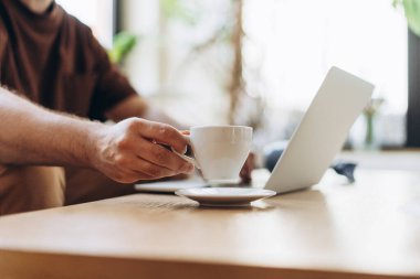 Yakın plan, meşgul yöneticinin portresi, dizüstü bilgisayar kullanan programcı, klavyede yazan yazar, kahve bardağı tutan, masaya oturan, ellere odaklanan. Kavram kır