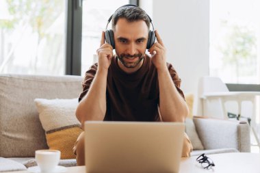 Mutlu, gülümseyen bir adamın portresi, kulaklık takan programcı, müzik dinleyen, dizüstü bilgisayar kullanan, modern ofiste çalışan, müzik dinleyen. Çevrimiçi teknoloji kavramı