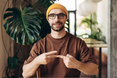 Ofiste şık sarı şapkalı ve gözlüklü, işaret diliyle konuşan, kameraya bakan kendine güvenen Latin sağır adam. İletişim konsepti