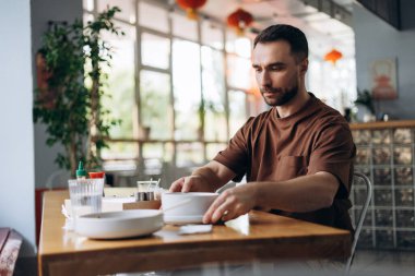 Modern kafede masada oturmuş Tayland yemeği yiyen yakışıklı, sakallı adamın portresi. Yiyecek konsepti