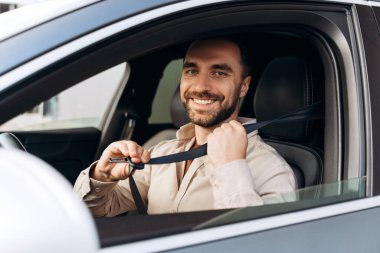 Yakışıklı, sakallı, kemer tutan, yeni arabada oturan ve kameraya bakan İspanyol adamın portresi. Ulaşım, sigorta kavramı