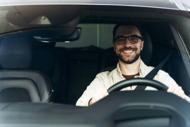 Çekici, orta yaşlı, gözlüklü, modern araba kullanan ve kameraya bakan Latin iş adamının portresi. Sigorta konsepti